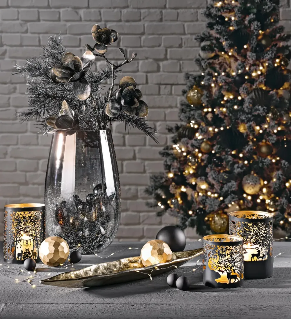 Festliche Weihnachtsdekoration Weihnachtsdeko mit silberner Vase, goldenen Kugeln, Kerzen und Tannenbaum mit Lichtern im Hintergrund.