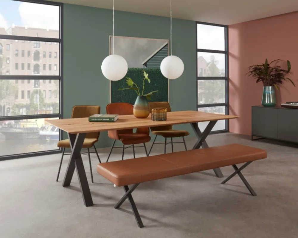 Trendige Essgruppe mit Lederbank und Holztisch in urbaner Loft-Atmosphäre mit farbiger Akzentwand. Moderne Essgruppe mit Holztisch, braunen Lederstühlen und Bank vor farbiger Wand und großen Fenstern mit Stadtblick