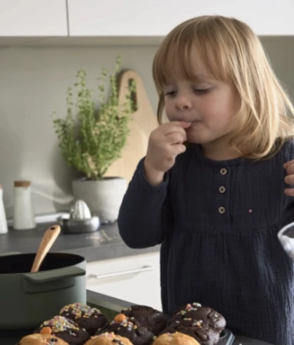Kind nascht Muffins in moderner Küche Mädchen isst Muffin neben Arbeitsplatte mit frisch gebackenen Muffins