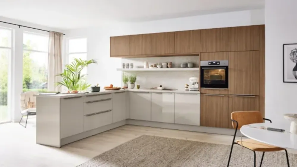 L-Küche Holz L-förmige Küche mit matten Fronten in Sand und Holzoptik, offenem Regal, Einbaubackofen und viel Tageslicht durch Fenster.