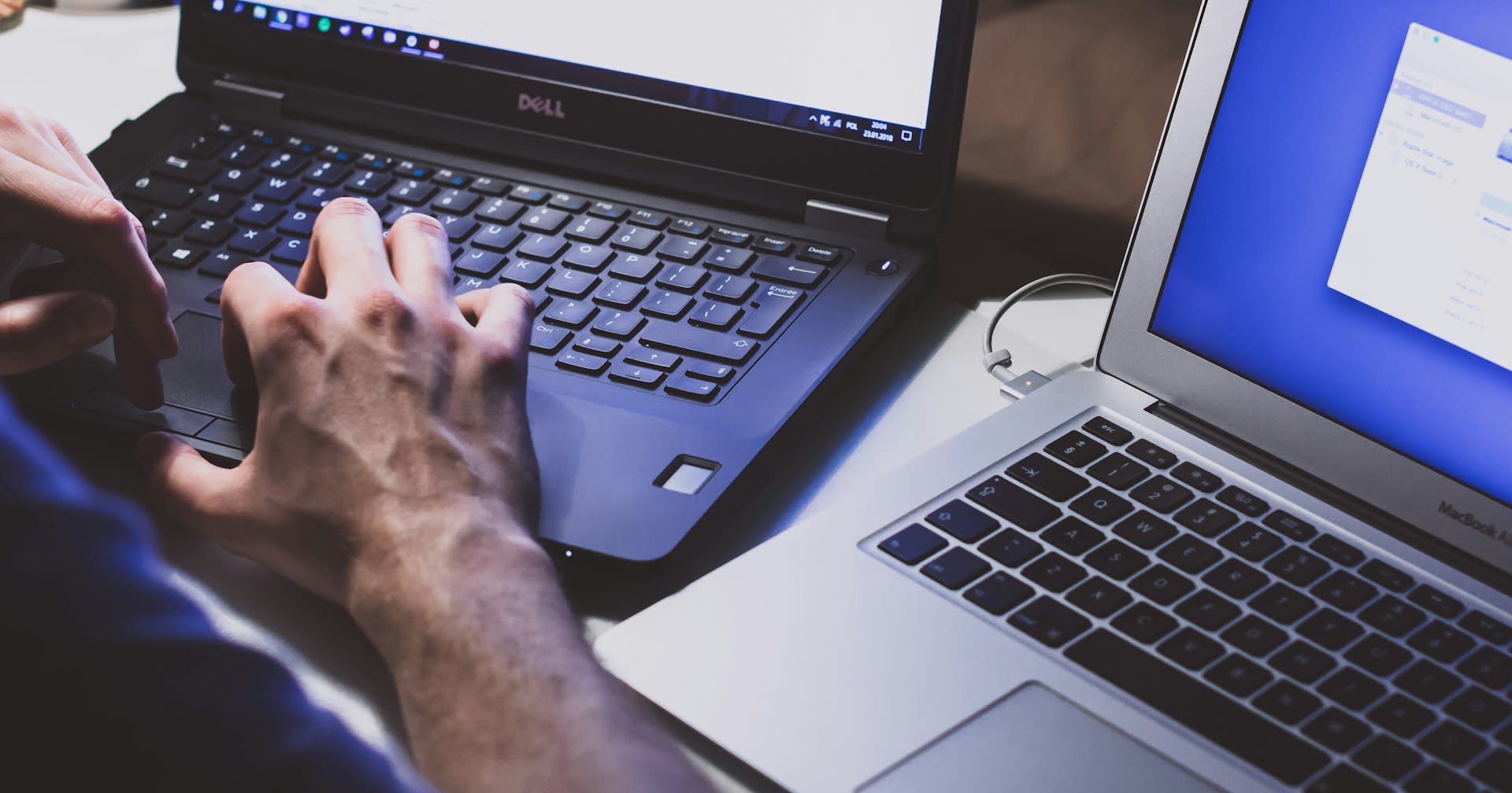 Someone typing on a work laptop with a second machine open alongside