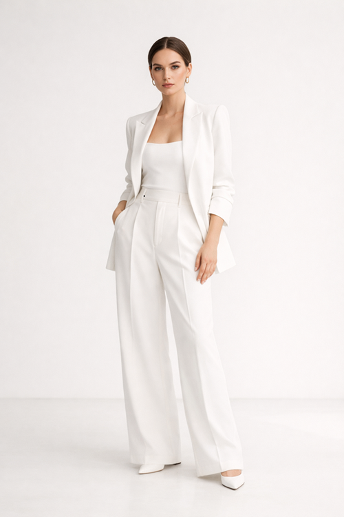 Female fashion model in a minimalist studio wearing a modern all-white outfit with soft shadows, clean background, and a calm editorial expression
