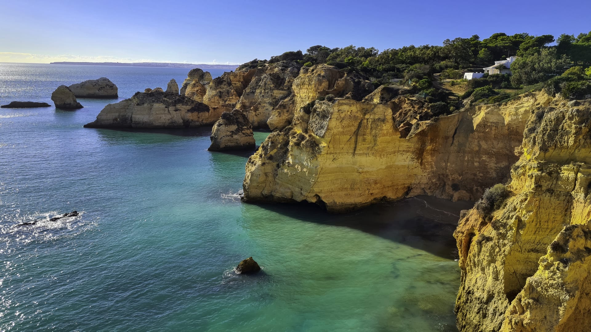 Turquoise ocean water between tall limestone rock formations at Praia da Marinha on a clear sunny day