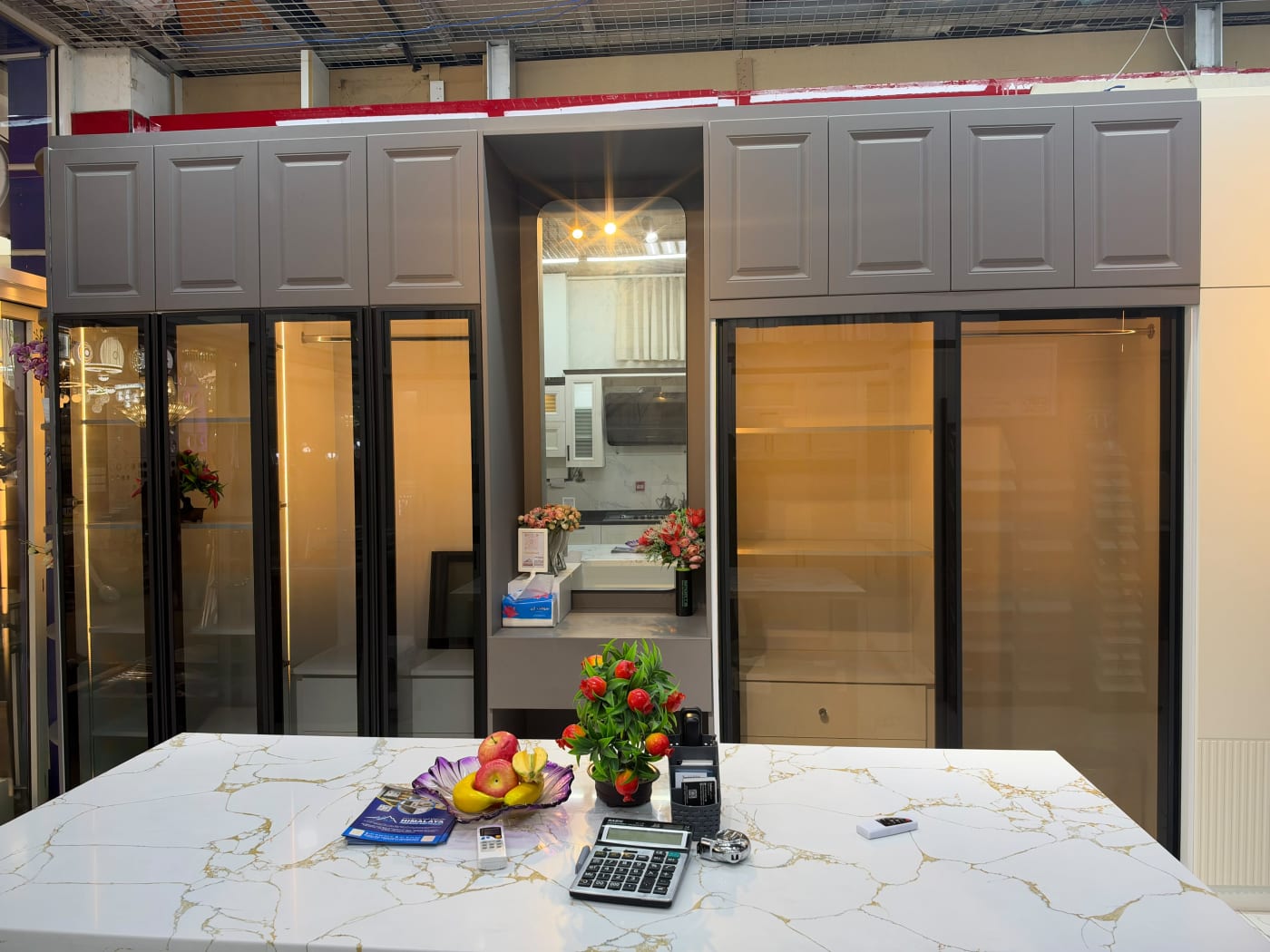Showroom wardrobe with black-framed glass doors, illuminated interiors and a central mirror and dressing shelf