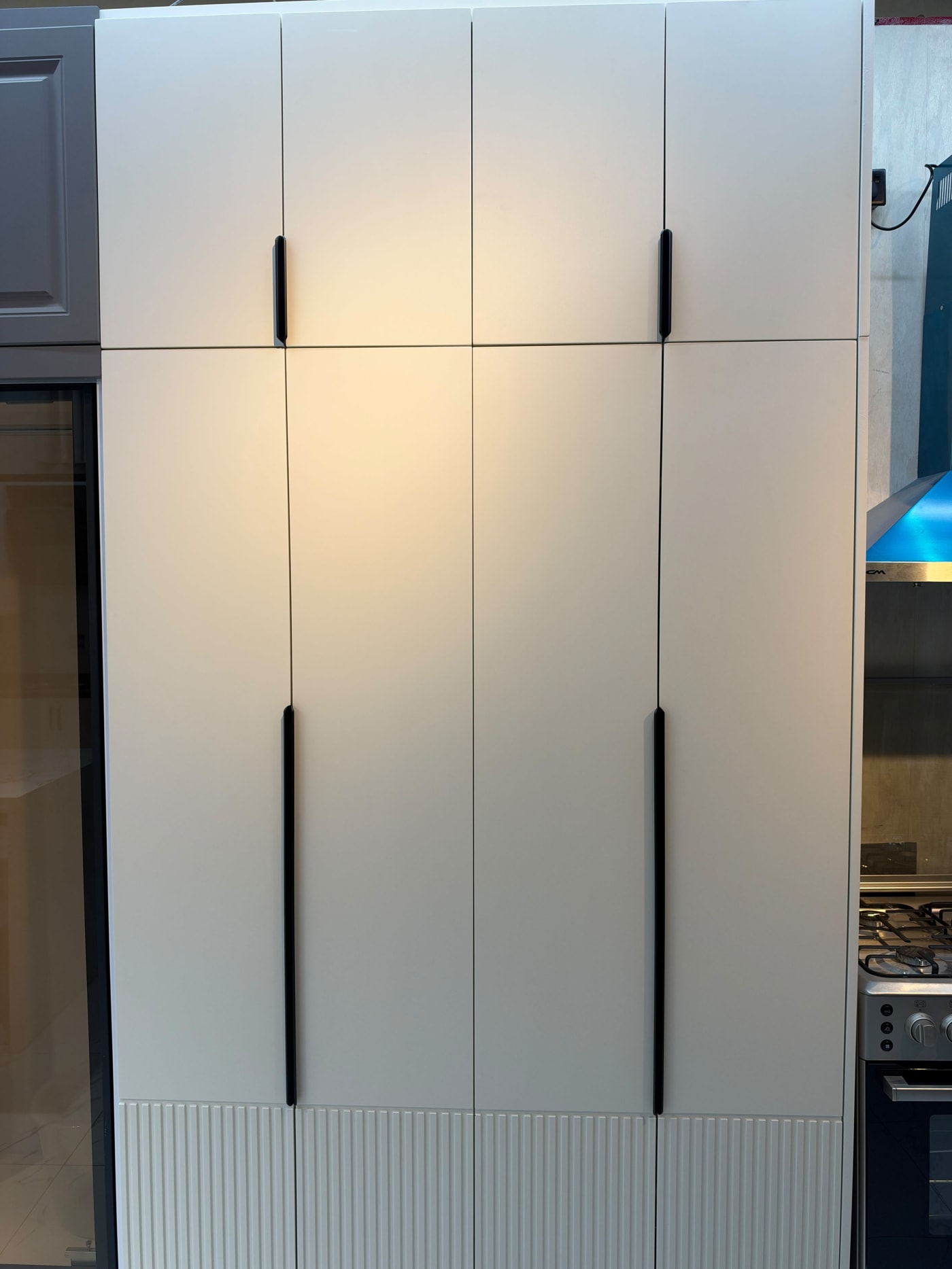 Full-height cream cupboard display with long black handles, overhead storage and fluted lower door panels