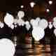 Many balloons float above a dark street - the balloons are lit like light bulbs.