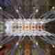 A photo looking directly up at the large hall of la Sagrada Família. There are 8 main support columns that radiate outwards.