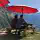 Ed and Oj sat at a picnic bench half way up a valley. There’s a large red awning above them.