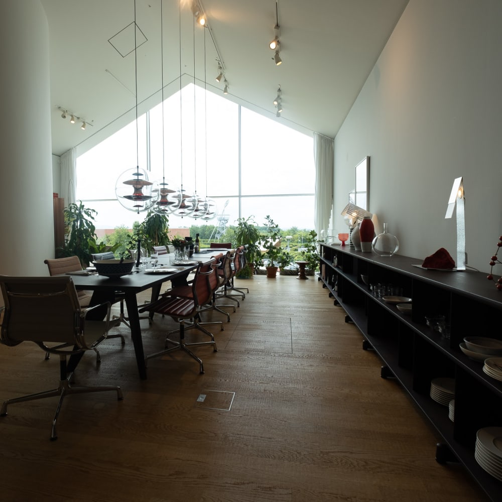 Looking towards a window inside the Vitra showroom. The room has a profile like a house with a pointed roof. Inside the room is a long table and bench.