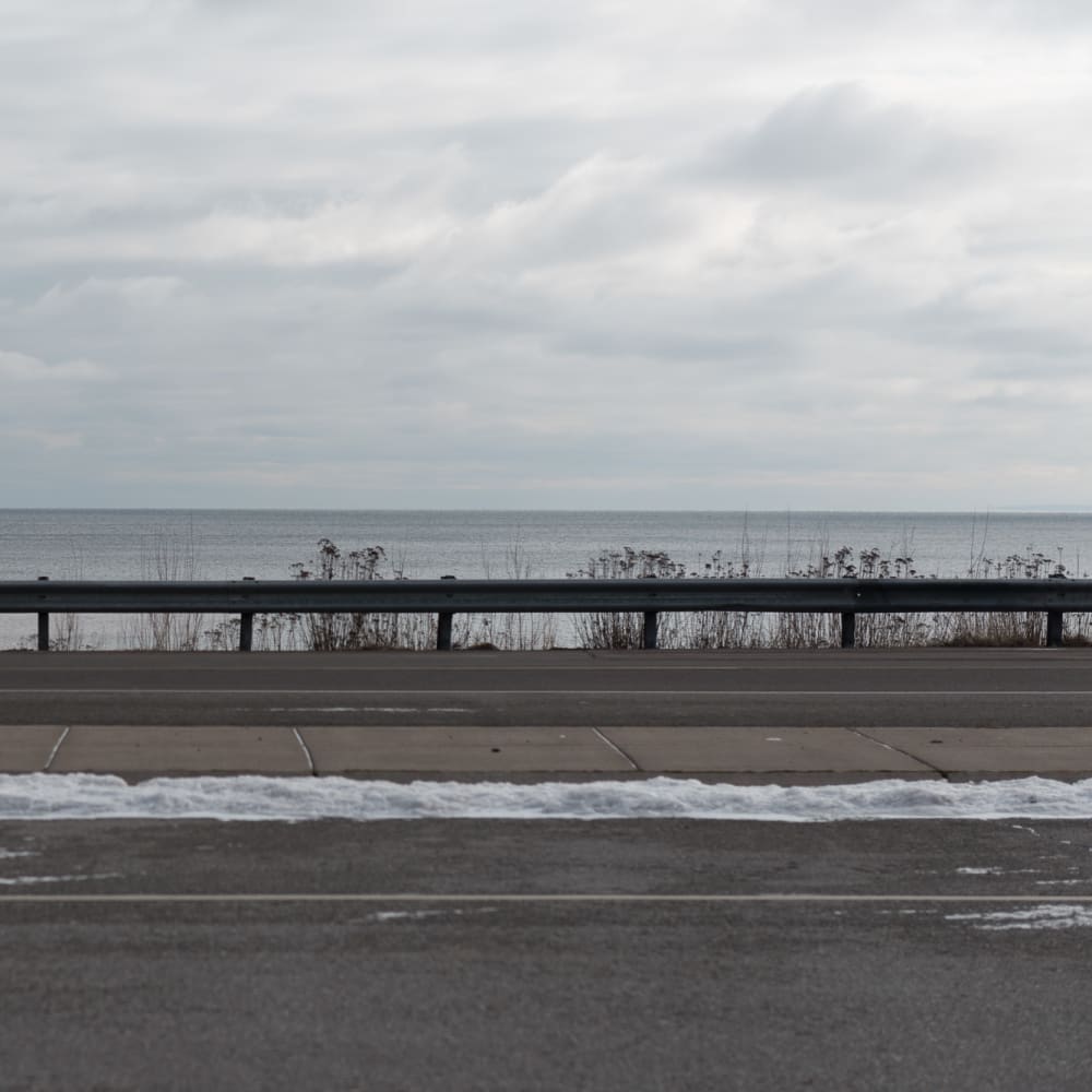 A photo from the side of a highway looking over the side. Lake Superior is in the background.