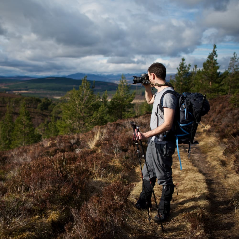 Chris taking a photo looking down a sunny hillside. There’s dark clouds in the background.