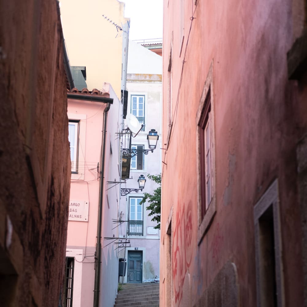 Looking up a narrow alleyway filled with two flights of steps. The buildings on each side are painted in light pink pastel colours