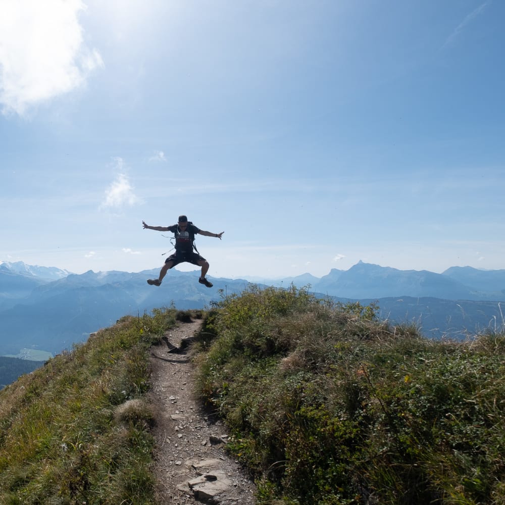 Oj in the air, mid jump. He’s high up on a mountainside in the bright sun.