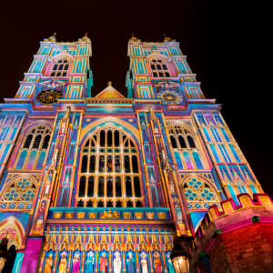 A photo of the front of Westminster Abbey at night. The entire front is lit up in bright pastel colours.