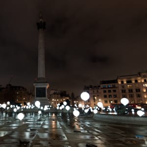Many balloons float above the ground of Trafalgar Square - the balloons are lit like light bulbs.