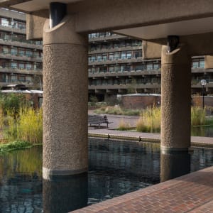 A photo of a Barbican walkway with a pond in the foreground.