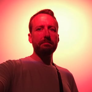 A self portrait of Ed Horsford. There’s a very bright red spotlight next to his head on the wall behind.