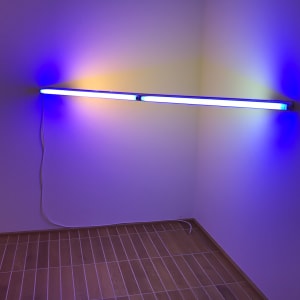 Photo of a light sculpture by Dan Flavin in the Kunstmuseum. The sculpture is a long fluorescent bulb stretching between two walls in the corner of a room. The bulb is the only source of light, and gives of a blue and white light.