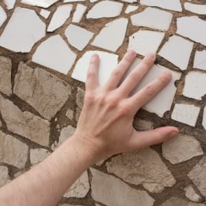 A hand rests on a large mosaic of broken white tiles.