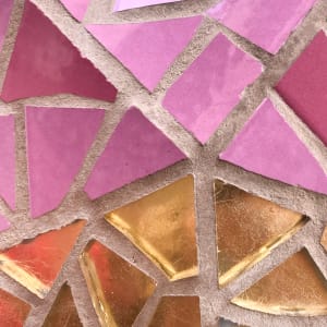 A close up of some tiled mosaic on the exterior of la Sagrada Família. The tiles are arranged in five segments like a pie chart. The top three segments are pink, and the bottom two are gold.