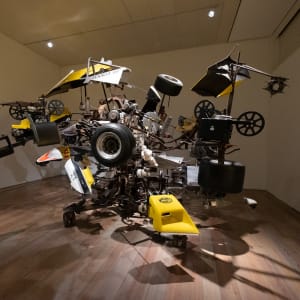 A large mechanical metal sculpture in a room - made from several car parts.