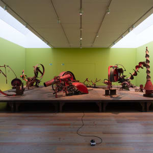 Wide photo of pale green room with several red mechanical sculptures in the middle.