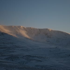 A wide panorama of a snowy mountainside as the sun sets.