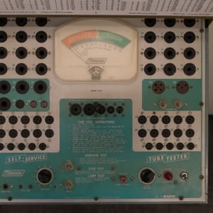 A photo of the front of a vintage ‘tube tester’. The camera is looking directly down on a control panel. There’s dials and inputs all over, with a large swinging gauge in the center.