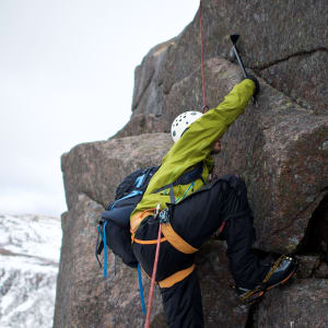 Chris takes a big step out on to an exposed section of Fiacaill ridge. His axe is in a crack providing support.