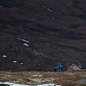 Long shot of several ski mountaineers in a valley. They have skied to the end of the snow, and are now packing up their gear.