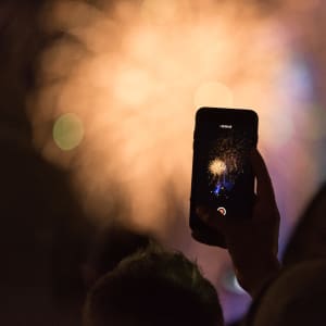 A phone is held taking a photo of fireworks in the distance.