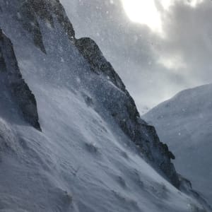 A snowy mountainside and valley, with swirls of snow in the air.