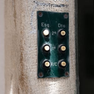 A macro photo of a set of doorbells on the wall. There are 6 white buttons on a dark green base.