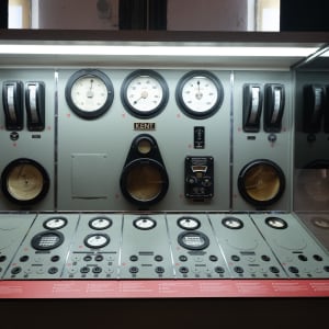 Looking straight on to a large control panel in Maat. The panel has a several columns of controls and dials and has a light grey-green surface colour.