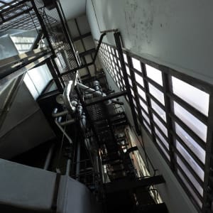 Looking up at the ceiling of the Maat engine room. There’s various walkways crossing the room and tall thin glass windows going up to the roof.