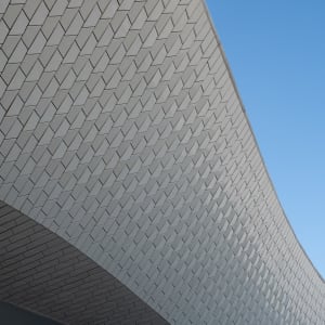 A close cropped detail of the Maat ceiling. the ceiling is in a flowing curved form and covered in small tiles. A cloudless sky can be seen behind.