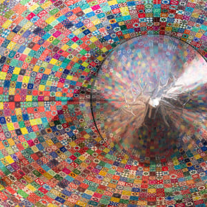 A round silver cone points directly at the camera. Iit is surrounded by a colourful mosaic print. It reflects some of the colours from the print.