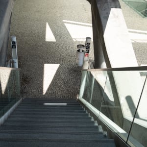 Looking down a staircase in a train station. The base of the stairs has an irregular tiled pattern.
