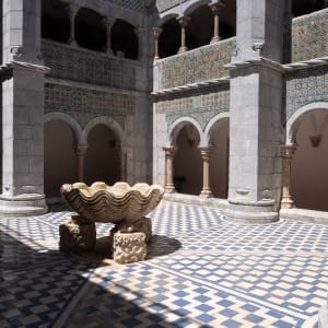 A view of the open-air courtyard in the centre of Pena Palace. The courtyard has blue and white checkerboard tiles, and a large fountain in the shape of a shell in the center.