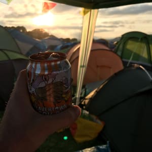 Holding a Beavertown beer can in golden sunset by a group of tents.