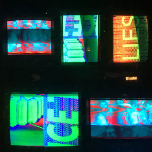Several vintage TVs stacked together display abstract brightly coloured slogans.