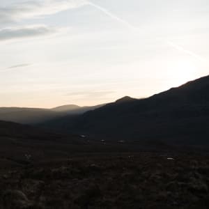 A photo of a valley in Torridon, just before sunrise. The sky is bright, but the land very dark still.