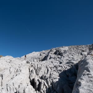 Oj climbs deeply creased rocks under a deep blue sky.