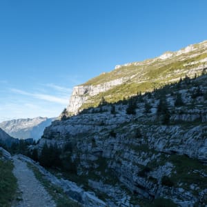 A photo looking down a valley in shadow as the sun sets. The right hand cliff is still lit brightly, in contrast to the dark blue rocks below.