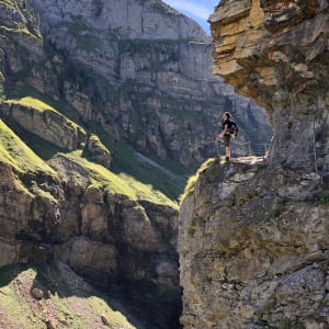 Ed holds a railing as he looks from one side of a steep valley to the other. The side he’s stood on has a near vertical wall of stone, with a path cut out in to it.