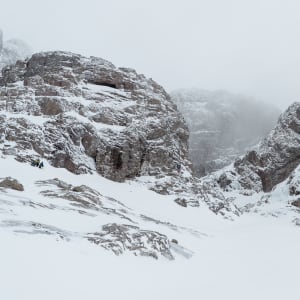 Some large rocky hills near Ben Nevis. They’re covered in snow and ice, and you can just make out small coloured figures dotted around them - people climbing the ice.