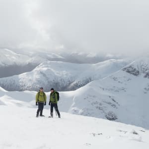 A portrait photo of Chris and Ed on top of a snowy mountain, with several other snowy summits visible behind.