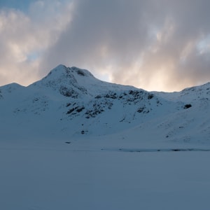 A panorama taken from the bowl of the Ring of Steall at dusk. The sky is still bright with dramatic clouds, but the mountains and ground around are getting dark.