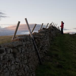 A stone wall recedes up and in to the distance. Chris stands at the far end looking out over one side.