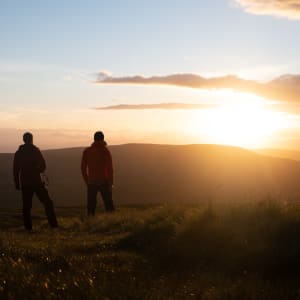 Ed and Chris stand in silhouette towards a very right and golden sunset.
